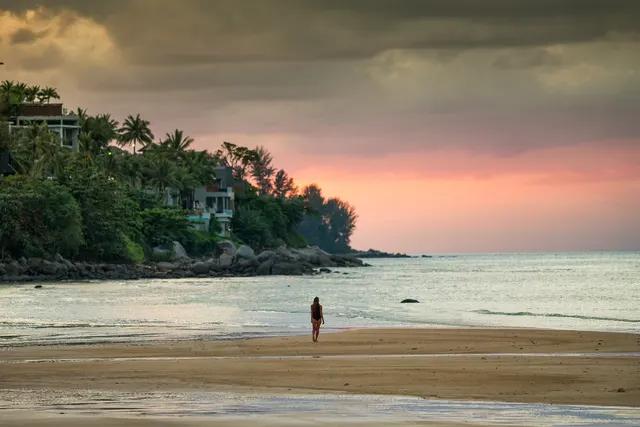 Kamala beach at sunset with a rocky headland and hillside villas among palms