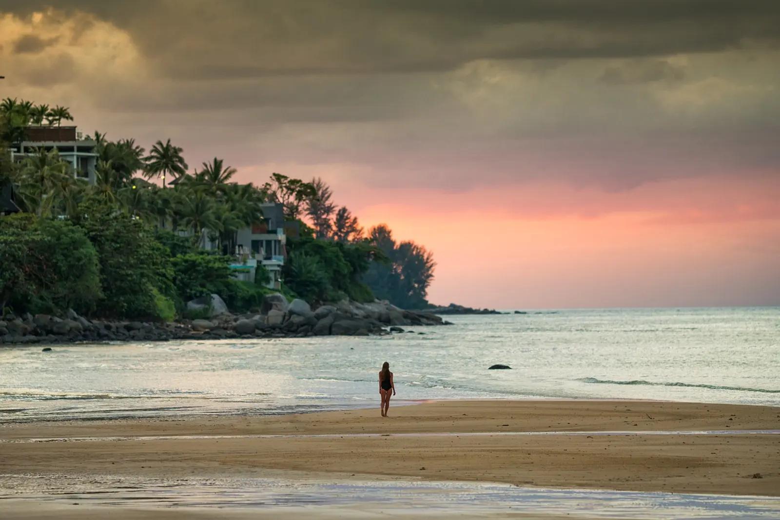 Kamala beach at sunset with a rocky headland and hillside villas among palms